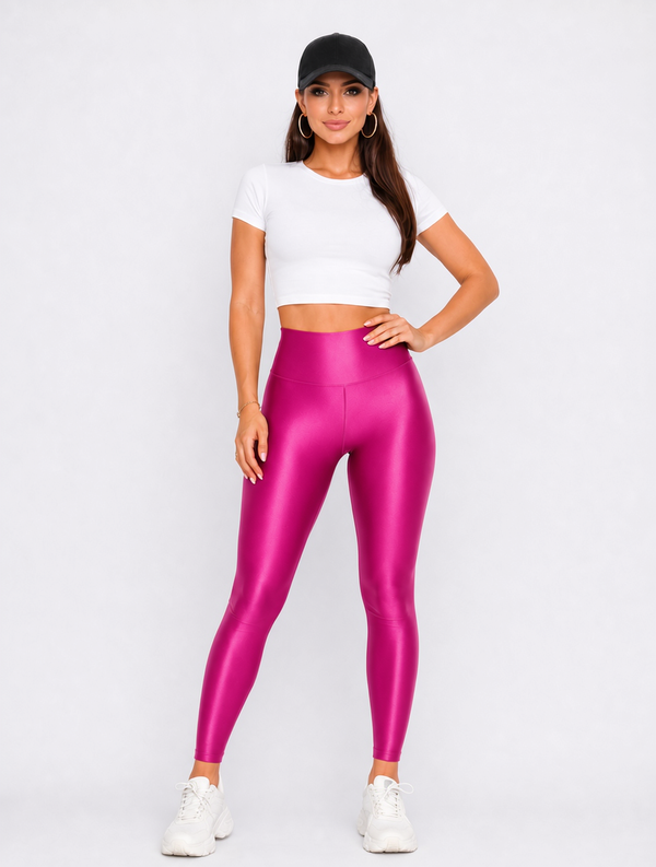 A woman modeling shiny metallic magenta-pink high-waisted leggings, paired with a white crop top, black baseball cap, and white sneakers, against a light gray studio background.