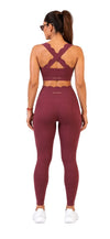 A woman shown from the back wearing a matching burgundy activewear set, featuring a sports bra with crisscross straps and high-waisted leggings, on a white background.