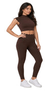 A woman modeling a matching brown ribbed two-piece activewear set with scalloped edges, featuring a mock-neck crop top and high-waisted leggings, paired with white sneakers.