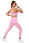 A woman modeling a light pink activewear set consisting of a sports bra with crisscross back straps and matching high-waisted leggings with scalloped hems, paired with white sneakers against a white studio background.
