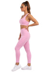 A woman modeling a light pink activewear set consisting of a sports bra and high-waisted leggings with scalloped hems, paired with white sneakers, against a plain white studio background.
