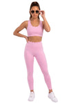 A woman modeling a matching light pink activewear set consisting of a scoop-neck sports bra and high-waisted leggings with a scalloped edge, paired with white sneakers and sunglasses against a white studio background.