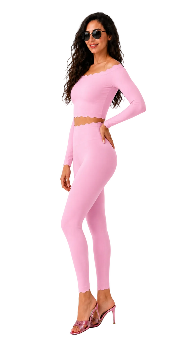 A woman modeling a light pink two-piece set consisting of a long-sleeve crop top with a scalloped neckline and matching high-waisted leggings with a scalloped hem, styled with clear high-heeled sandals against a plain white background.