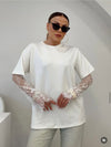 Person wearing a white oversized t-shirt with lace sleeves against a plain background