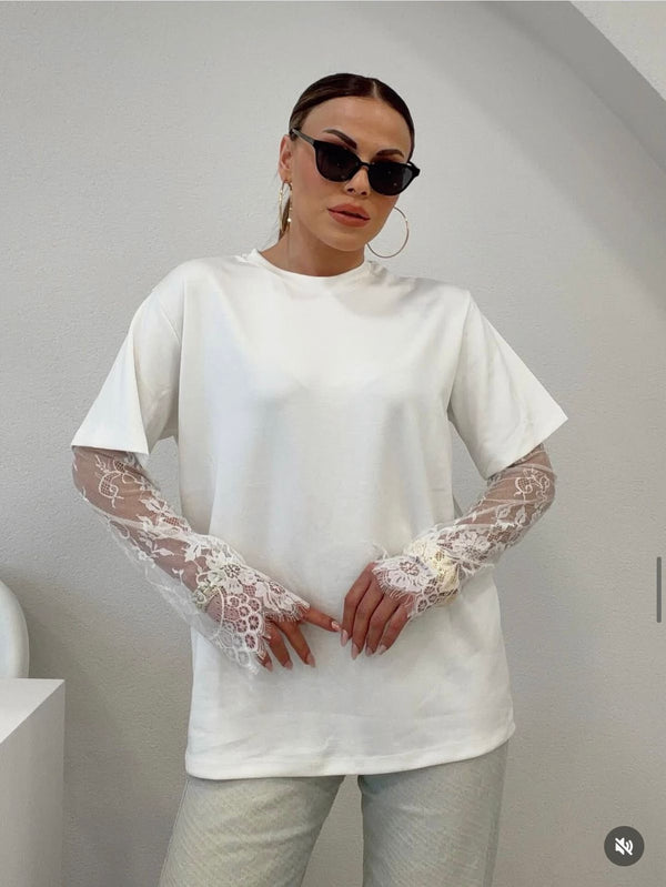 Person wearing a white oversized t-shirt with lace sleeves against a plain background